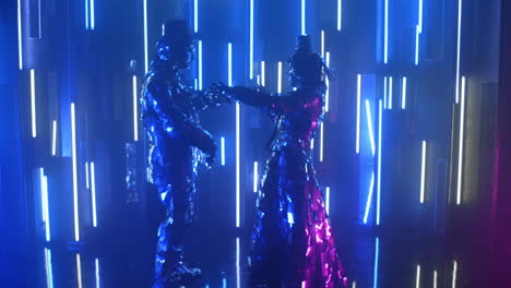 Zwei-Robotertänzer-In-Glitzernden-Kostümen-Tanzen-Vor-Einer-Neonwand-Und-Kommen-Einander-Näher.